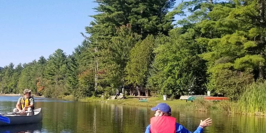 person in canoe educating other people in a canoe about invasive species on a pond