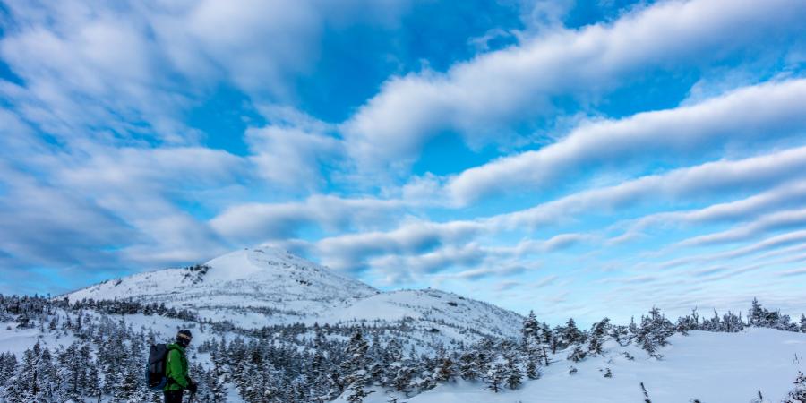 person snowshoeing up snowy mountain with blue sky and clouds above