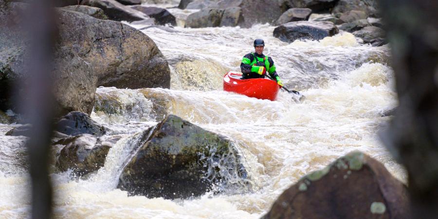 person paddling red canoe down rapids