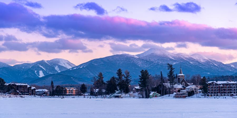 purple sunset over adirondack mountains taken from small lake with buildings around shore