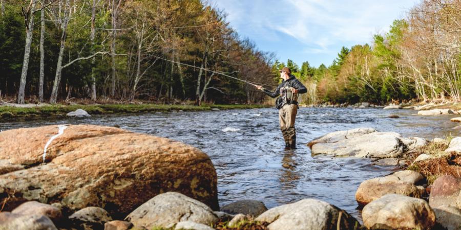 Man standing and fly fishing in middle of river during autumn