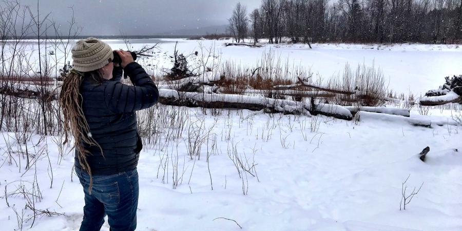 Woman using binoculars to view birds at snowy lake in winter