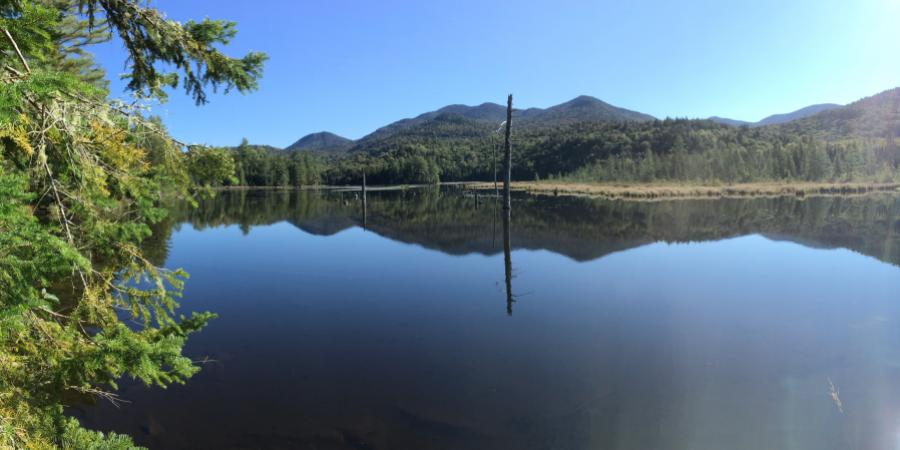 lake surrounded by forest and hills with blue sky above and sun shining down