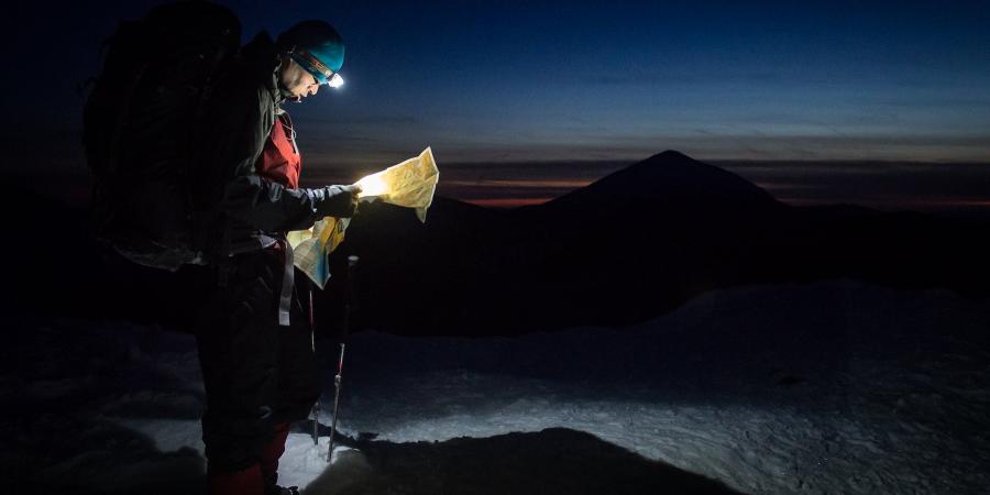 Winter hiker on the summit of a mountain looking at a map by headlamp