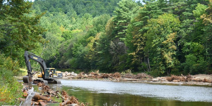 An excavator working in a river surrounded by forest